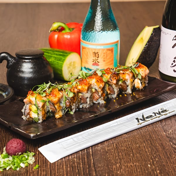 Sushi rolls with avocado and salmon, garnished with sprouts, alongside sake bottles and fresh vegetables.