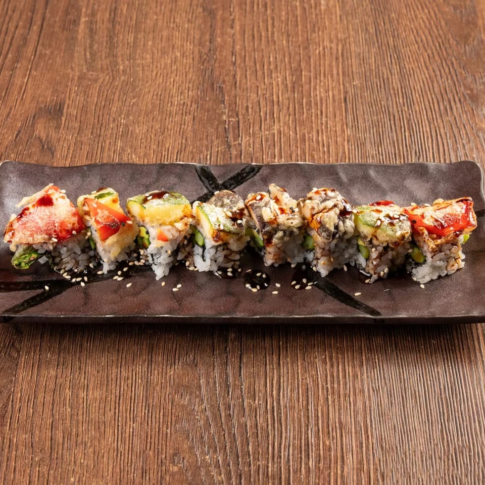 Eight pieces of colorful sushi with various toppings and sauces on a dark rectangular plate.