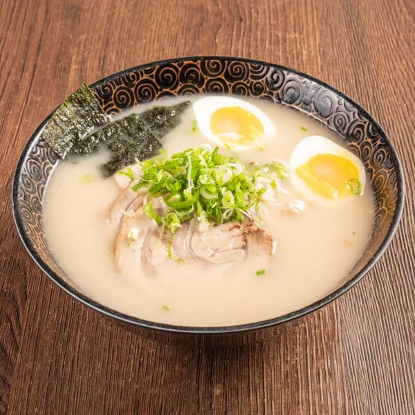 Ramen bowl with pork, green onions, nori, and two soft-boiled egg halves in a creamy broth.