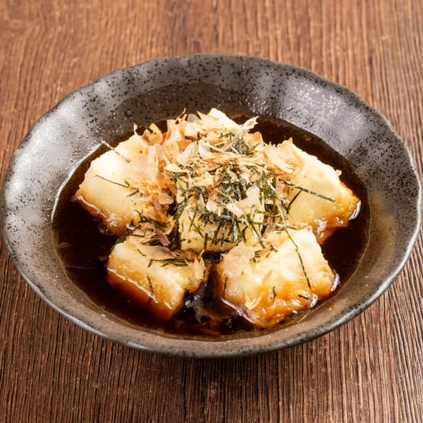 Agedashi Tofu, deep-fried tofu in a savory broth, topped with bonito flakes and seaweed.