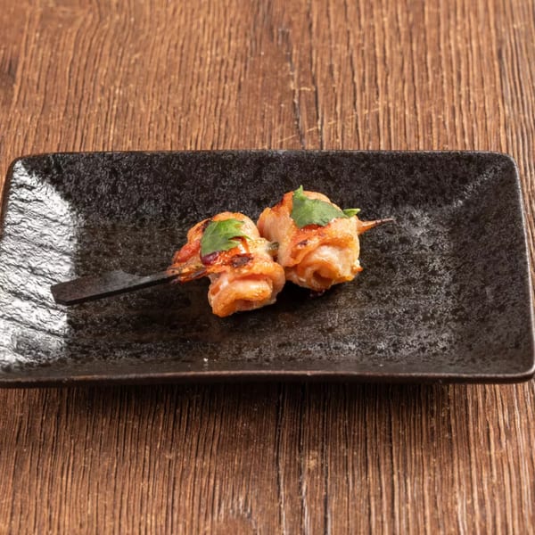 Two grilled shrimp skewers with green herbs on a rectangular black plate on a wooden table.