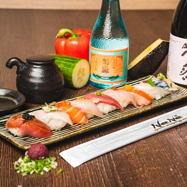 A platter of colorful nigiri sushi, sake bottles, and fresh vegetables on a wooden table.