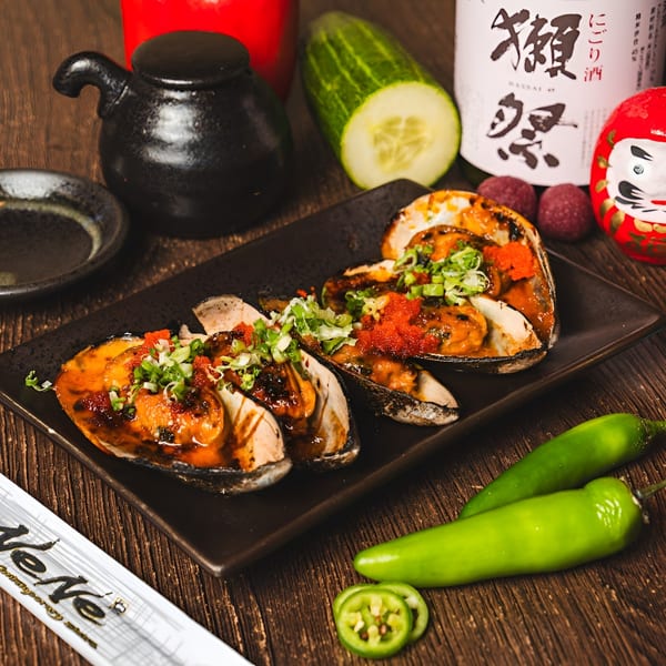 Baked mussels topped with roe and scallions, surrounded by Japanese condiments and fresh vegetables.