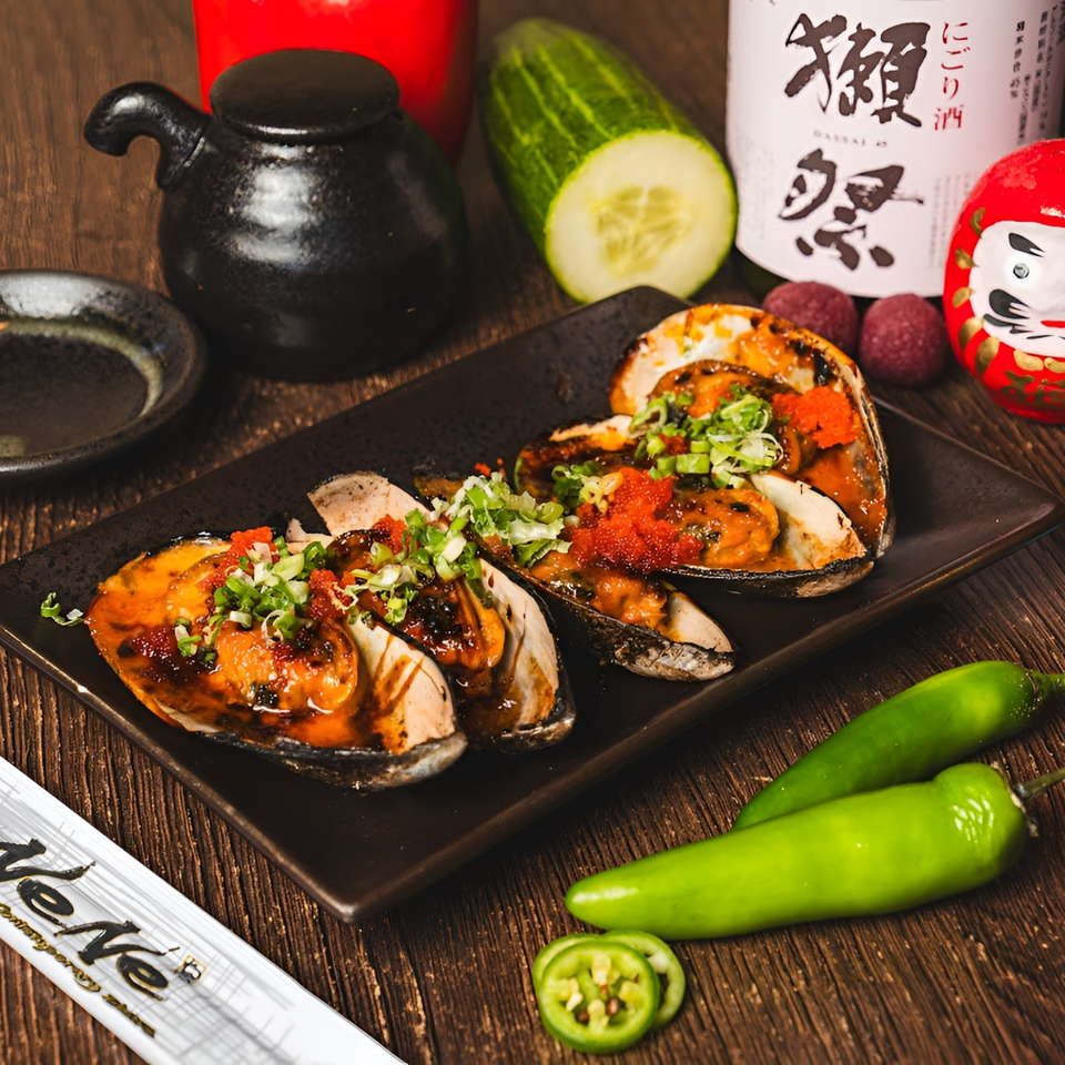 Baked mussels topped with roe and scallions, surrounded by Japanese condiments and fresh vegetables.