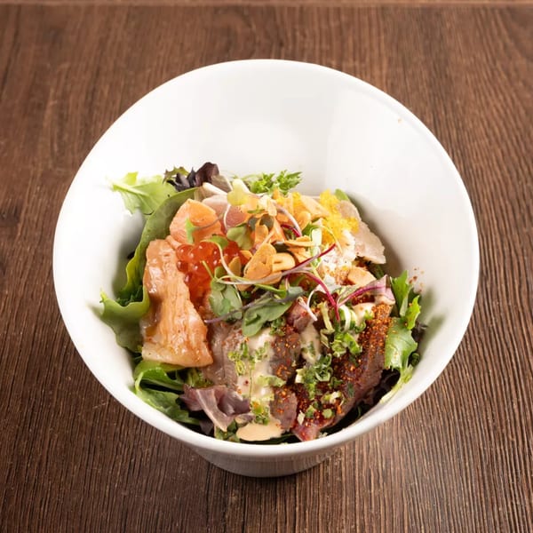 A white bowl filled with a colorful salad featuring greens, salmon, tuna, roe, and a savory dressing.