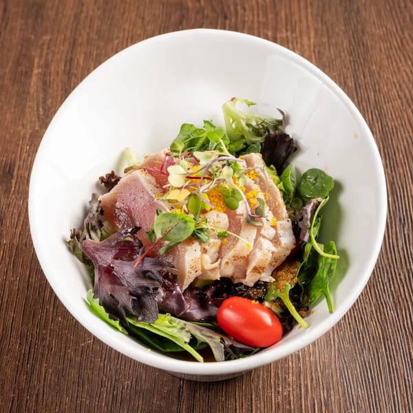 Seared tuna salad with mixed greens, microgreens, and a cherry tomato in a white bowl.