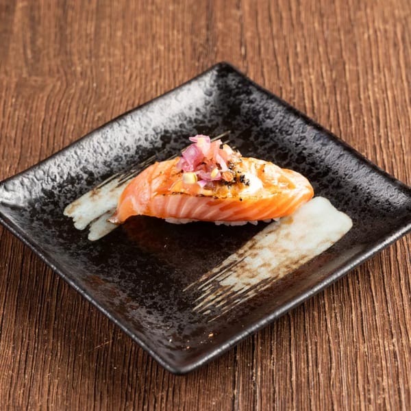 Close-up of a single piece of salmon nigiri sushi with red onions on a black plate.